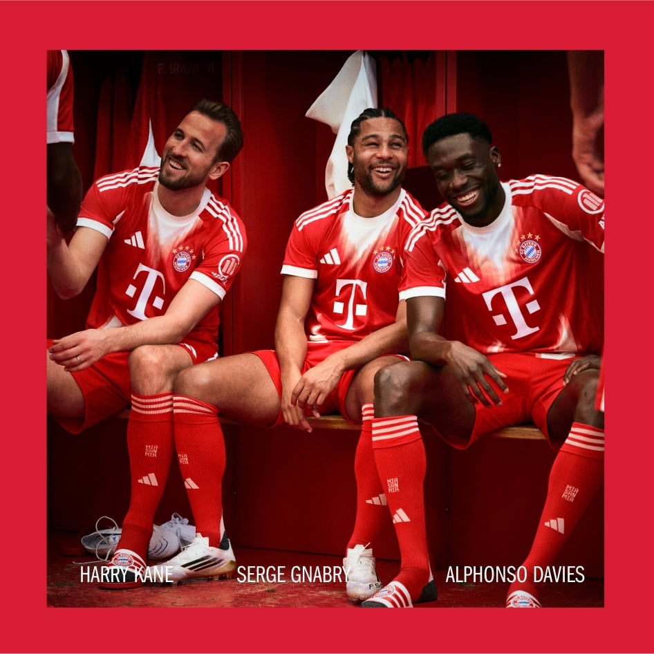 Three soccer players in red uniforms sitting together, with a red curtain or backdrop behind them.